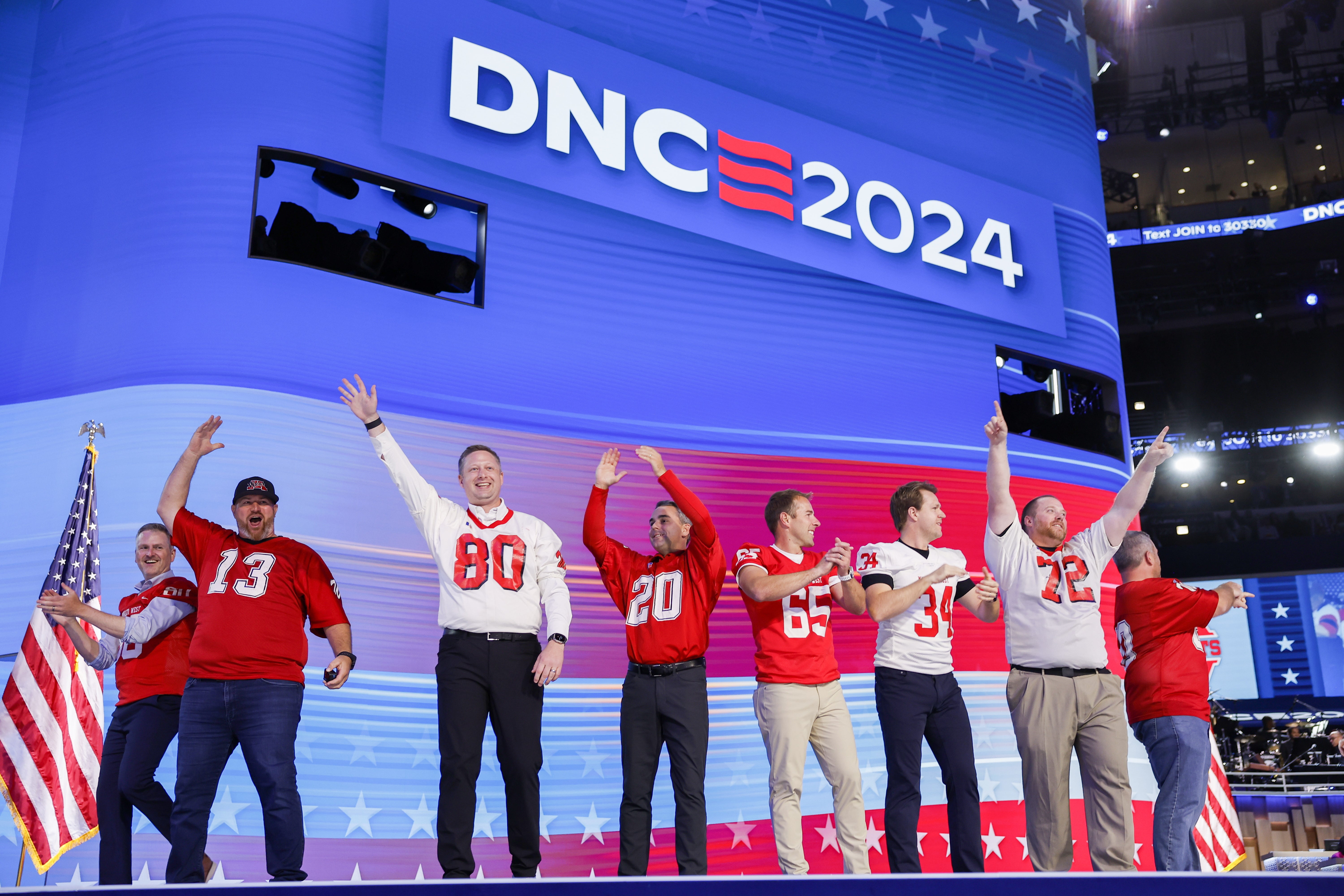 Former members of the Mankato West High School football team coached by Tim Walz wave to the audience on stage at DNC