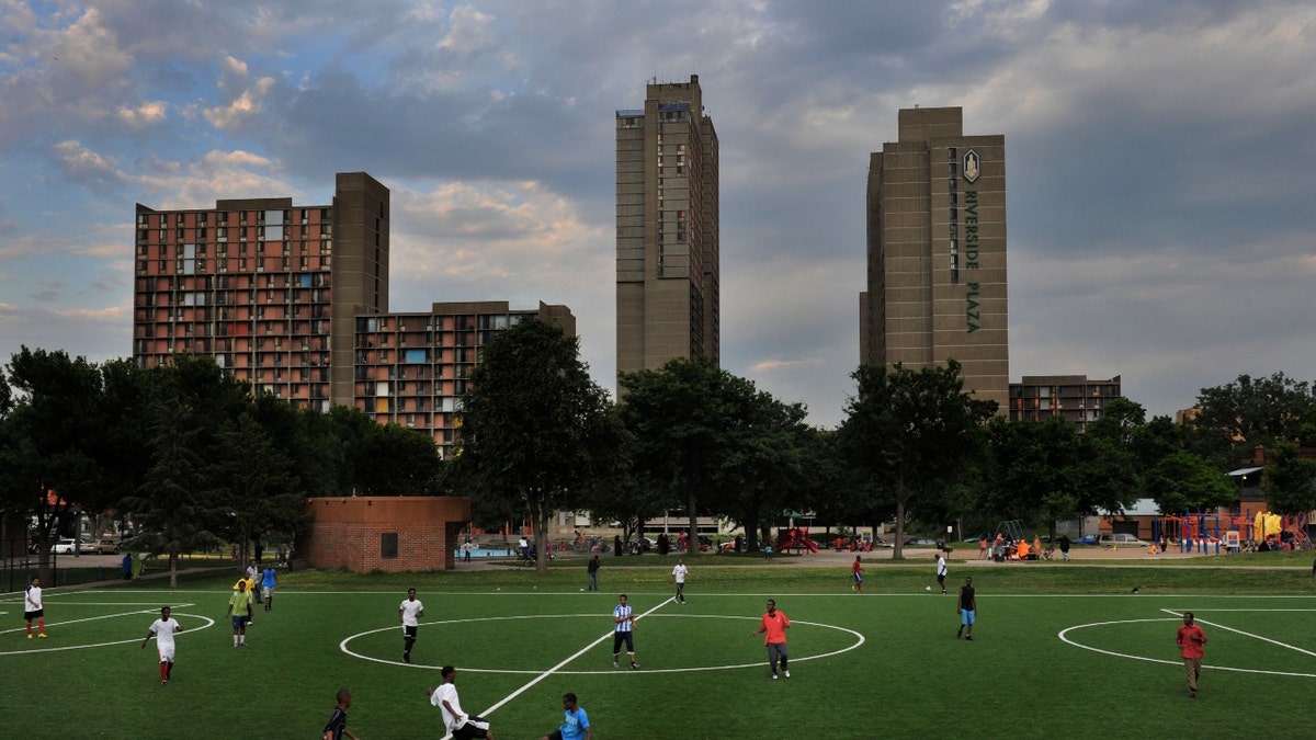 Young men play soccer as mothers and fathers socialize and parent their playing children in Currie Park next to the Cedar-Riverside apartment complex that houses mostly Somalis who have been displaced here starting in the early 1990's by their country's civil war on June 30, 2011, in Minneapolis, MN. 