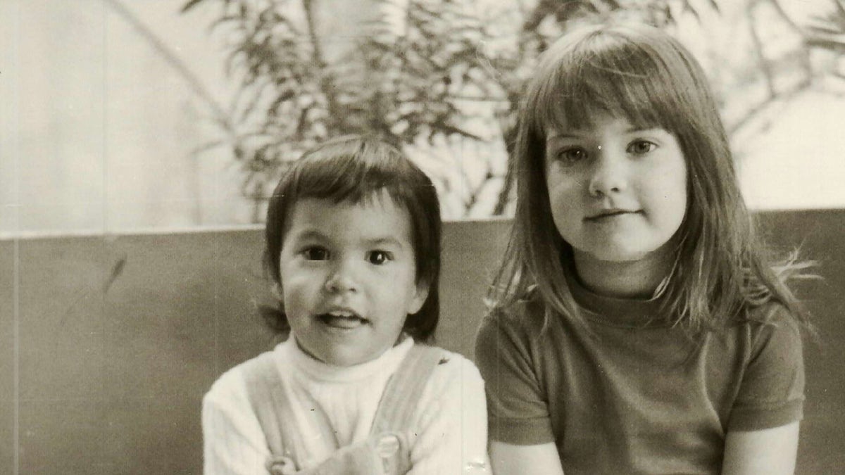 Jonelle Matthews wearing a white sweater and overalls posing next to her sister in a shirt.