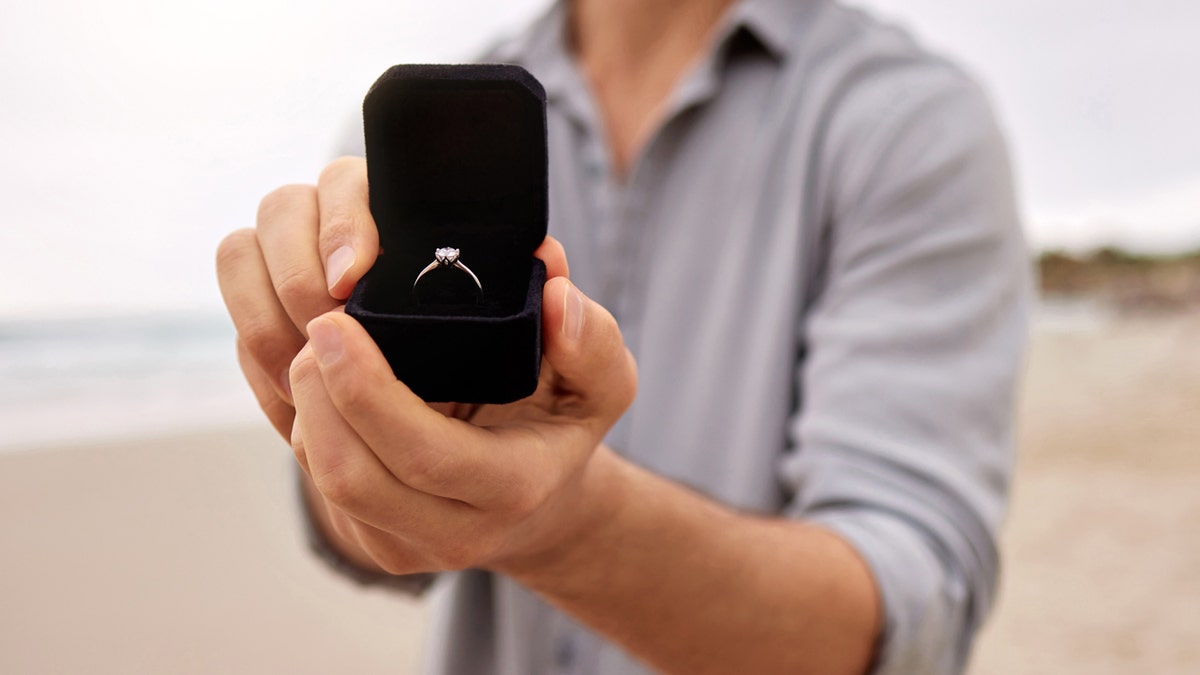 A man holding an engagement ring in an open box