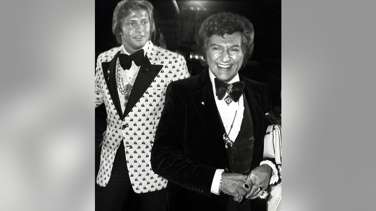 Scott Thorson in a polka dot suit walking behind Liberace who is wearing a suit and tux.