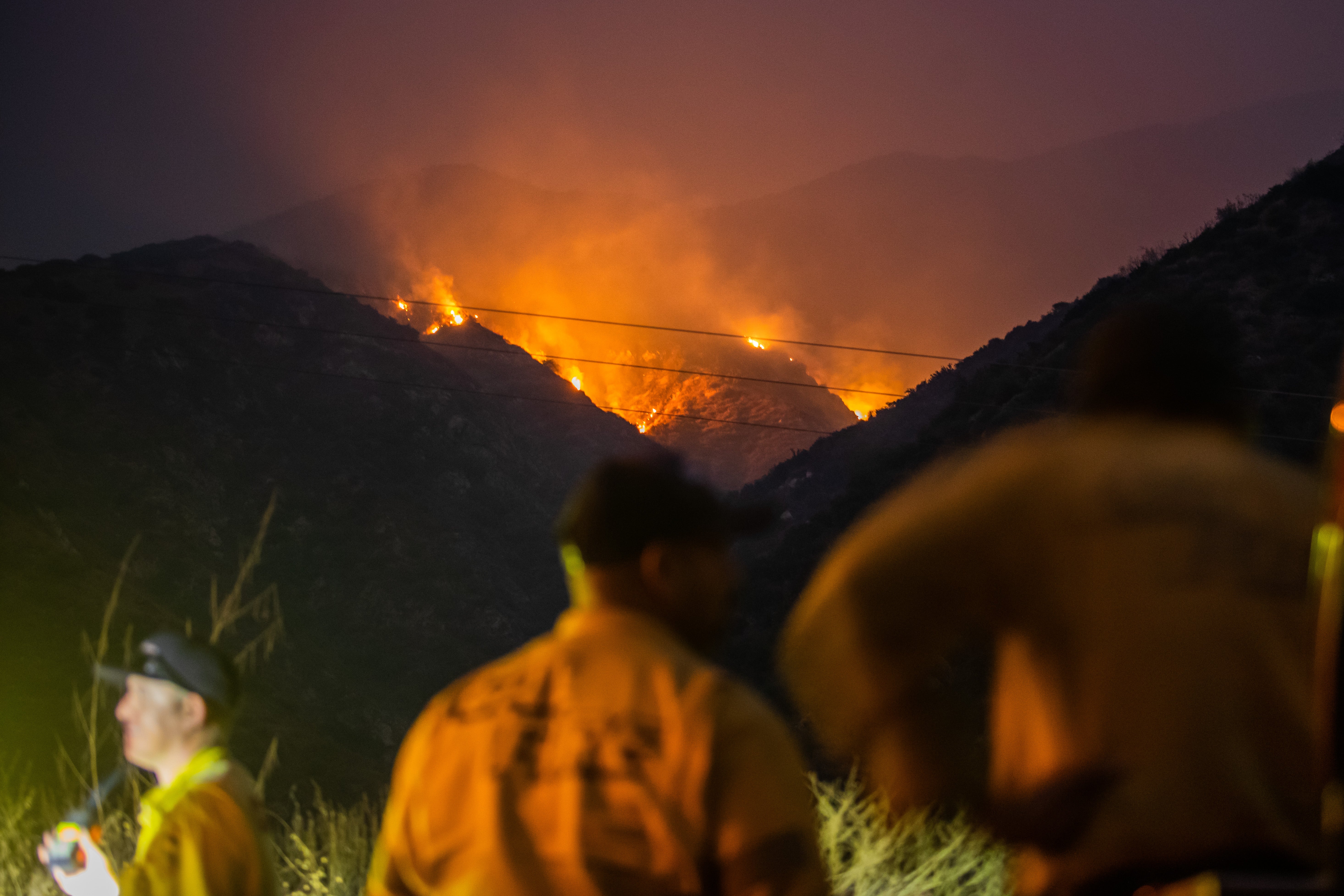 Firefighters watch as the Line Fire burns in the foothills of the San Bernardino Mountains on Sunday. The fire has forced evacuation orders for thousands of Southern California residents. Several school districts canceled school on Monday.