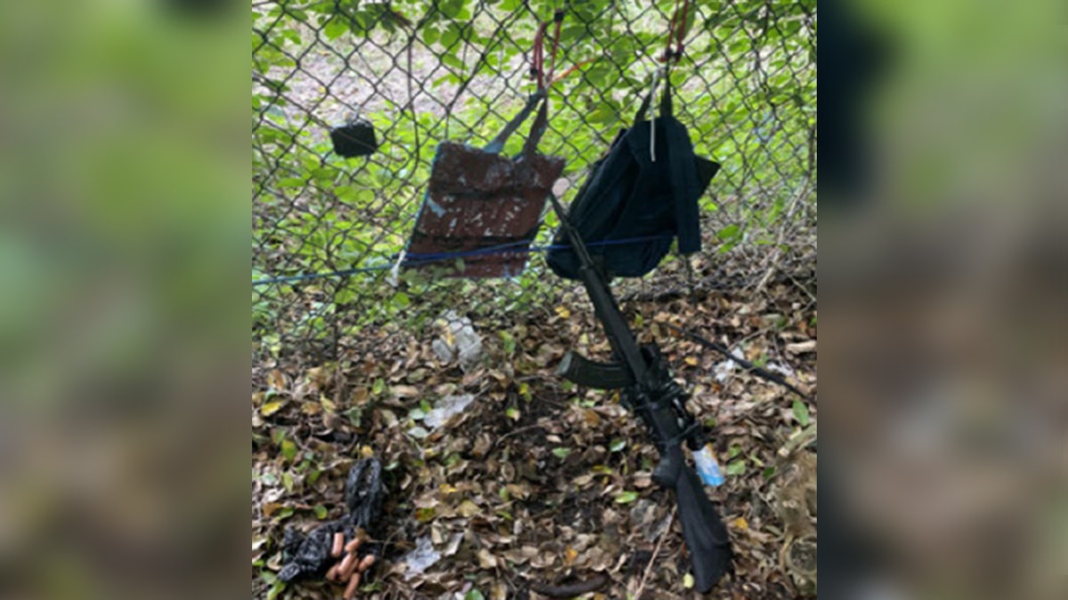 rifle aimed through fence with two bangs hanging nearby