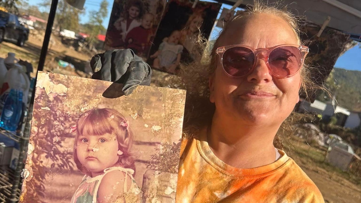 Dara Cody holds up a muddied photo recovered from debris after Helene