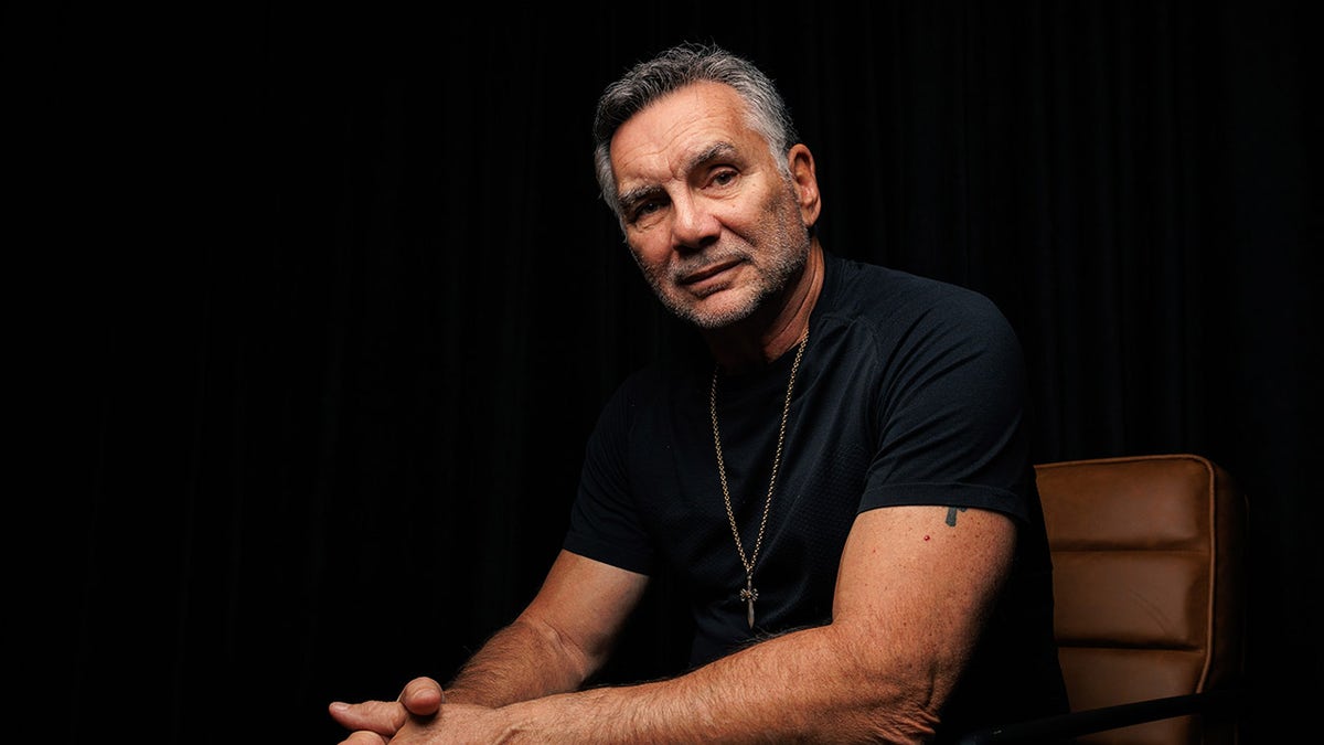 Michael Franzese wearing a black shirt and gold chain looking to the side.