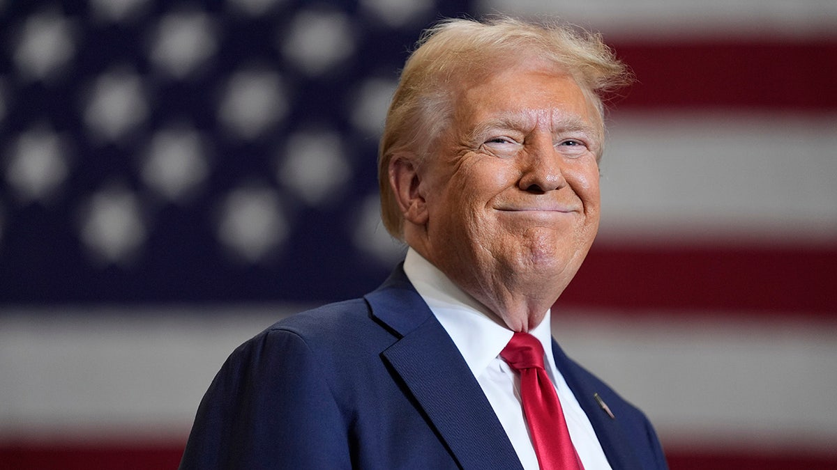 Trump smiling closeup shot, US flag behind him 