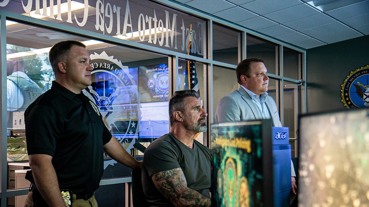 Lou Valoze sitting next to two officers facing a computer.