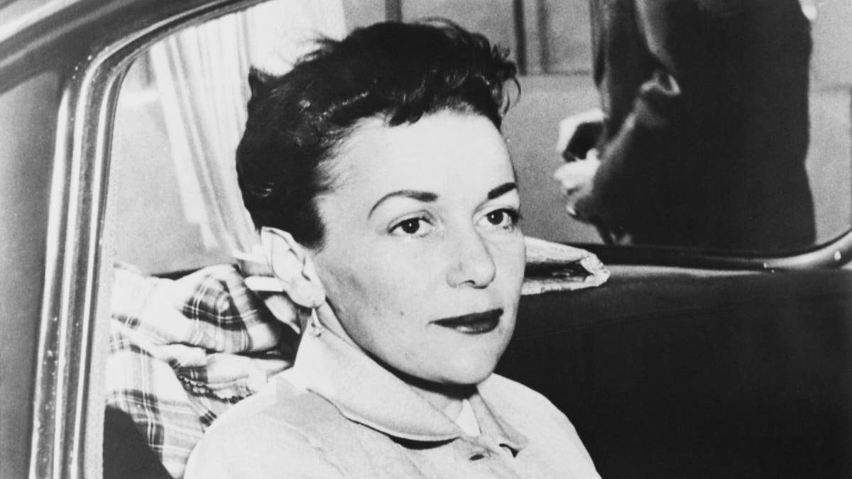 Barbara Graham Riding in a prison transport, black and white photo, with dark lipstick, her hair up, wearing a coat