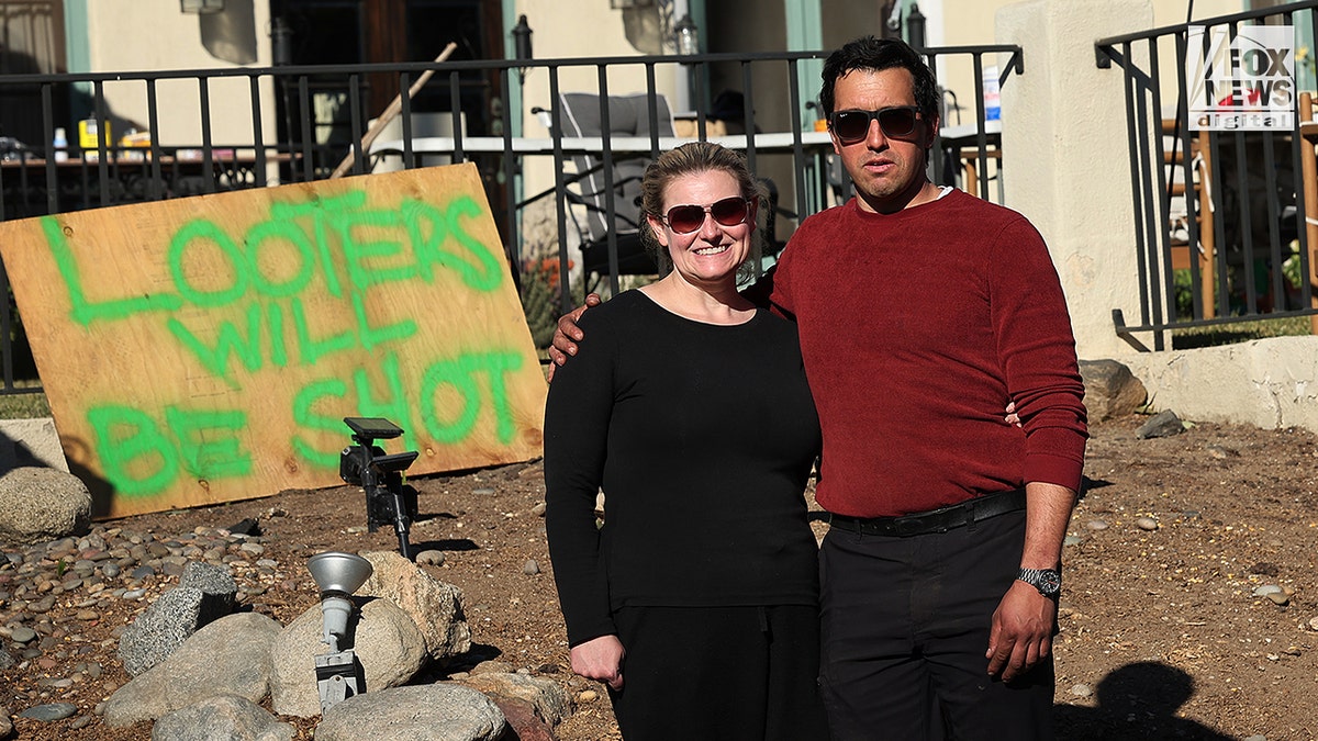 California fire survivors update, a couple stand in front of a sign posted to ward off looters.