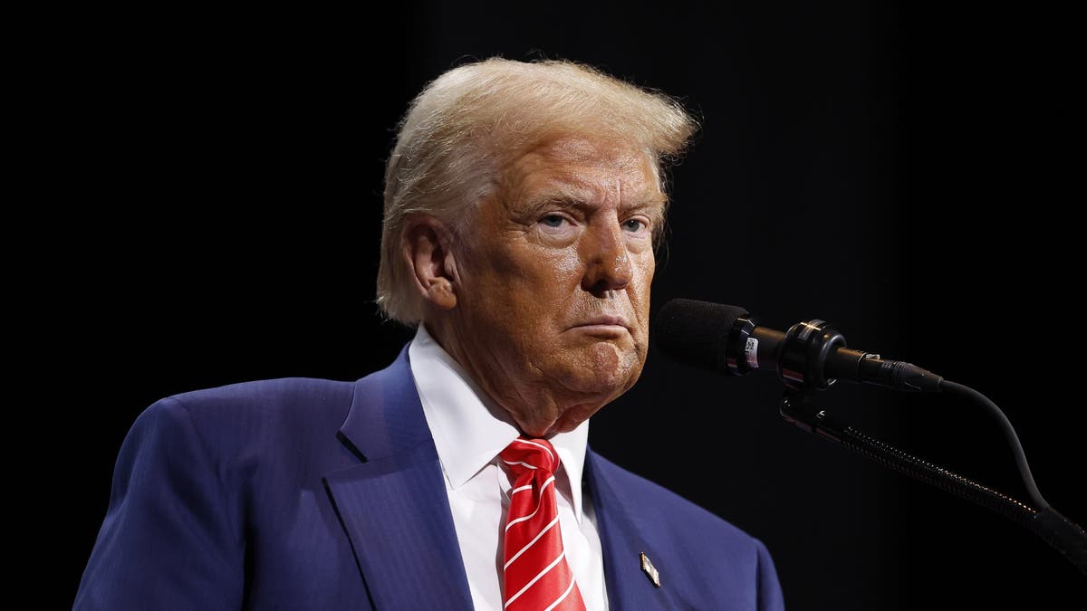 Trump speaks behind a microphone wearing a blue suit, white shirt and red tie