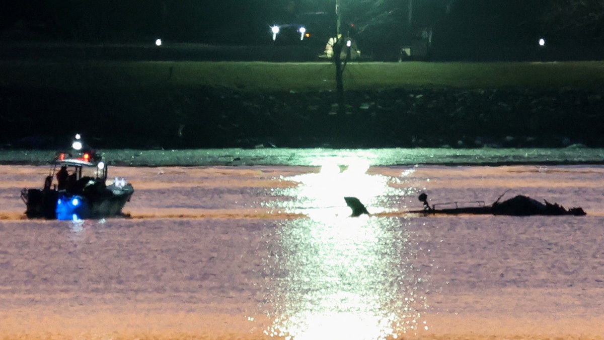 Rescuers on a boat work next to the wreckage of a Black Hawk helicopter at the site of the crash