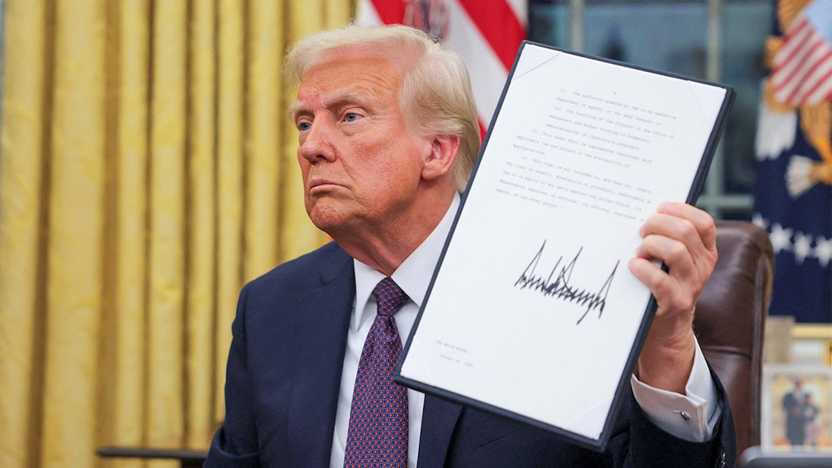 President Donald Trump holds up a signed document