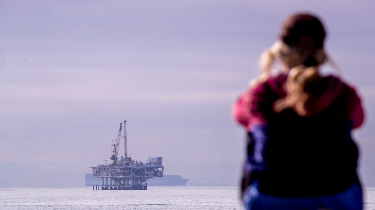 A person looks out over the ocean with a view of oil platform Esther and container ships