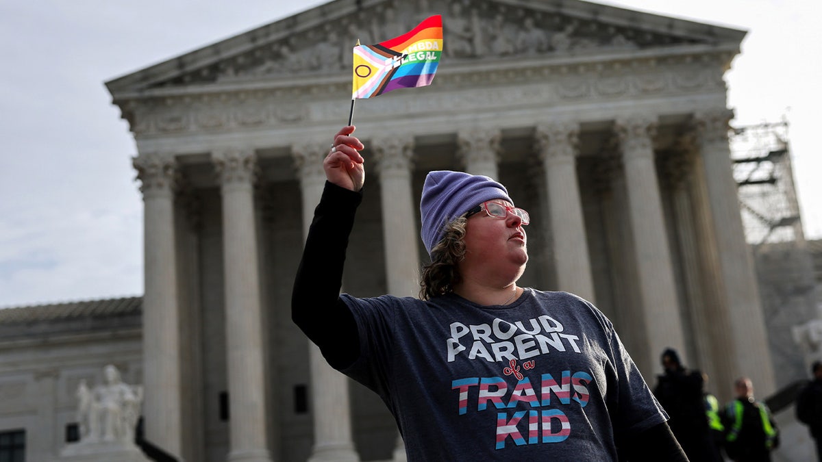 A transgender rights supporter protests outside the U.S Supreme Court building, waving an LGBTQ+ flag